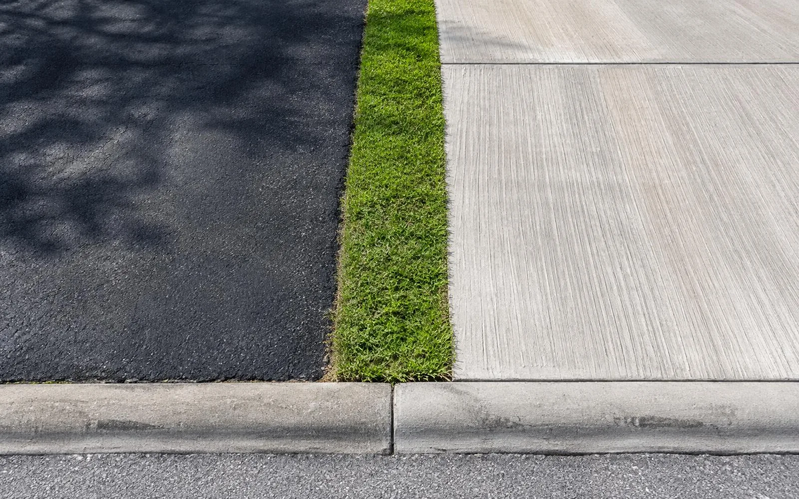 Asphalt and broom-finish concrete surfaces separated by a grass strip in Pembroke Pines