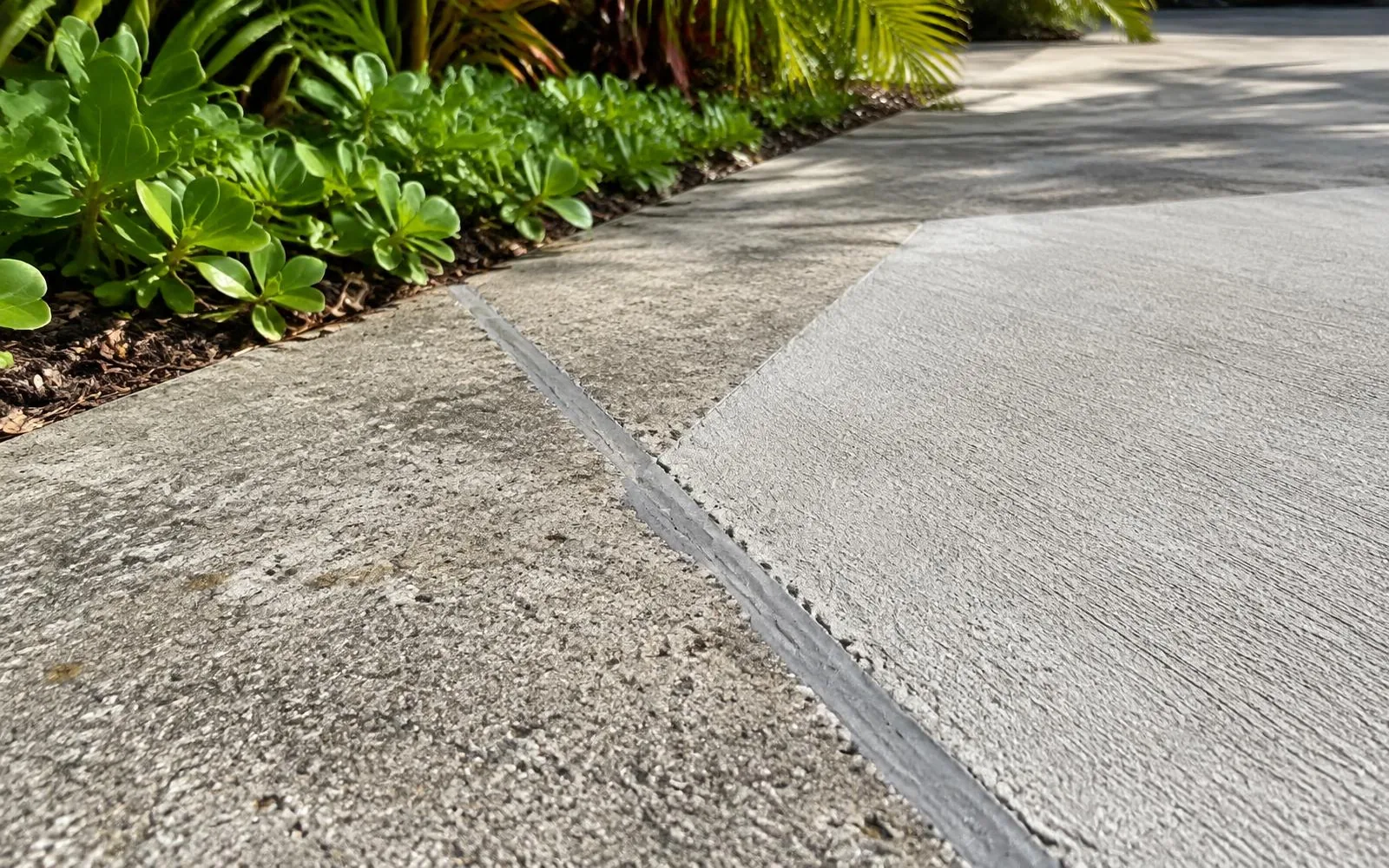 Sealed driveway crack beside a freshly resurfaced section and garden edge in Pembroke Pines
